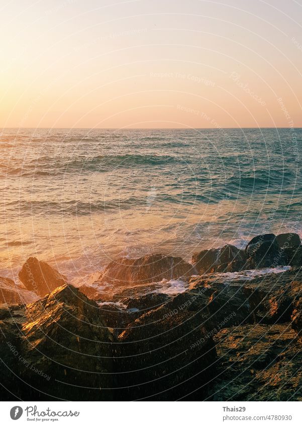 Bright sea sunset. The waves crash into the rock, lit by the warm sunset, sand and pebbles. Sea wave breaks into splashes and white foam. Wave splash at sunset.