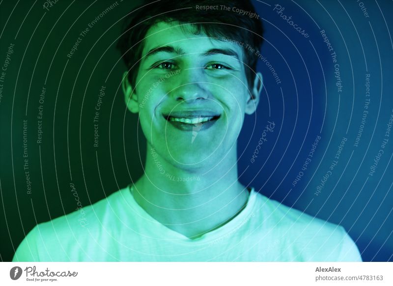 Portrait of young man with dimples in cheeks in green and blue light in front of petrol colored wall Boy (child) Man Young man younger Large pretty Strong