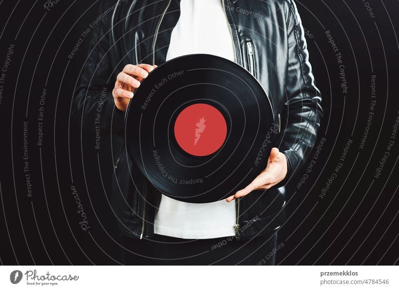 Man holding vinyl record. Vintage music style. Rock Style. Male wearing black jacket holding black disc standing on dark background. Retro music disco sound