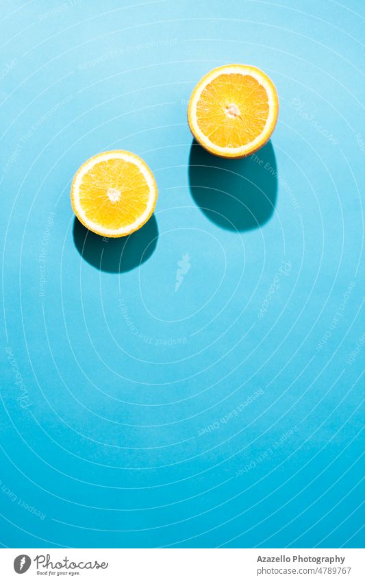 Simple concept flatlay two pieces of orange under the bright light with black shadows on blue background. diet pop art flashlight minimalism healthy food