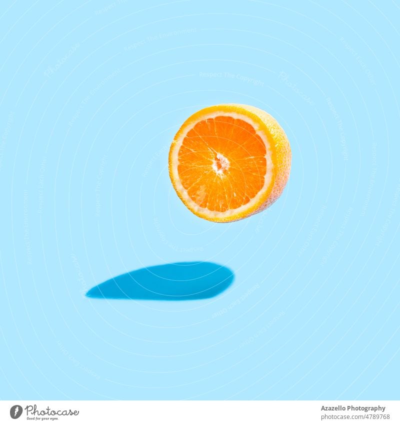 Isolated orange half with a real shadow on blue background. Flying orange on blue. minimalism still life detoxification healthy food vitamins slice delicious