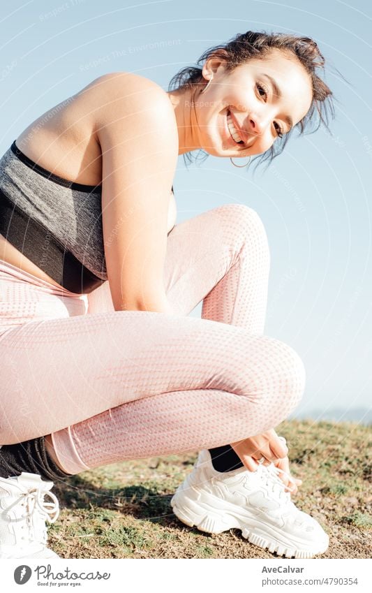 Young woman lacing her shoes while smiling to camera with copy space. Happy young people training during a sunny summer day preparing for the beach body. Training clothes.