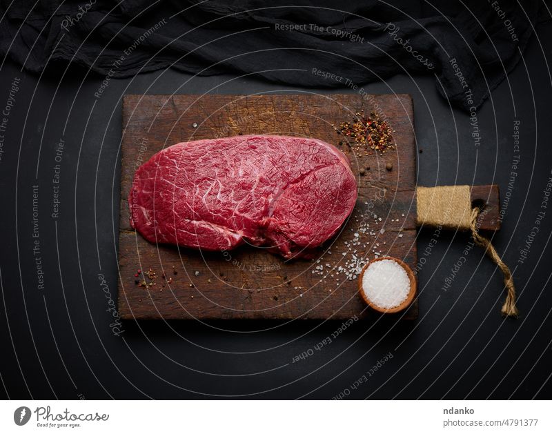 Raw beef tenderloin lies on a cutting board and spices for cooking on a black table, top view preparation banner beefsteak bloody butcher cow cuisine dinner