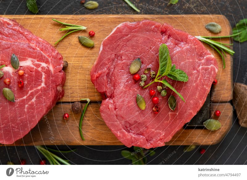 Raw beef fillet steaks with herbs and spices on wooden board on dark background close up meat food raw red fresh mignons uncooked nuts green copy space rosemary