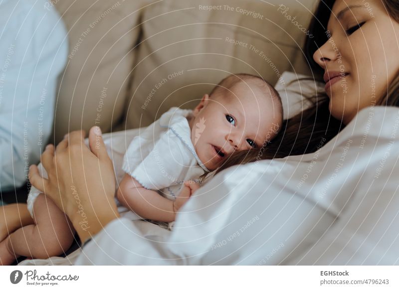 Newborn baby boy looking at the camera on top of his mother lying on the sofa newborn mom infant comfortable kid indoors bonding couch motherhood son