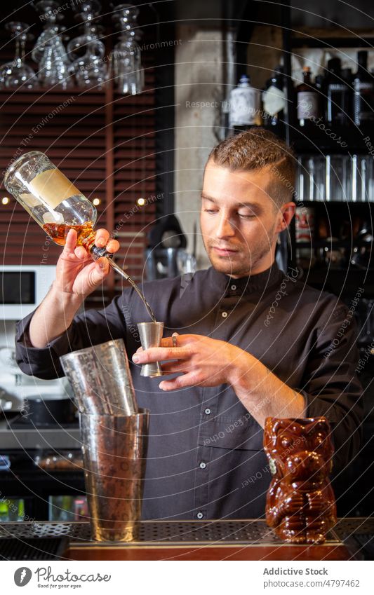 Professional barman pouring alcohol drink into jigger during cocktail preparation prepare bartender counter work male young uniform nightlife ron vodka