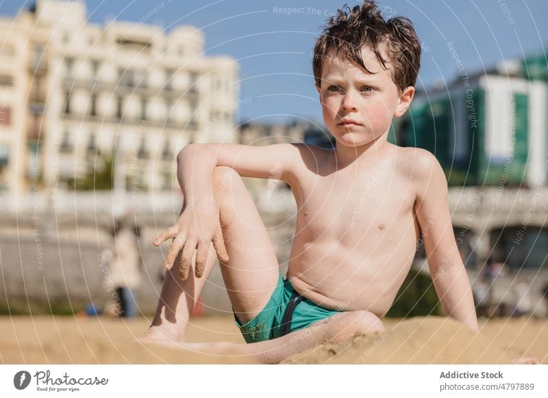 Thoughtful boy on sandy beach looking away kid summer coast childhood rest pastime sea shore recreation naked torso shirtless leisure cute appearance seashore