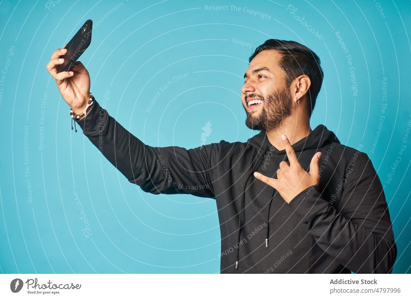 Cheerful man taking selfie while making sign of horns smartphone self portrait rock and roll social media style photography cellphone casual trendy confident