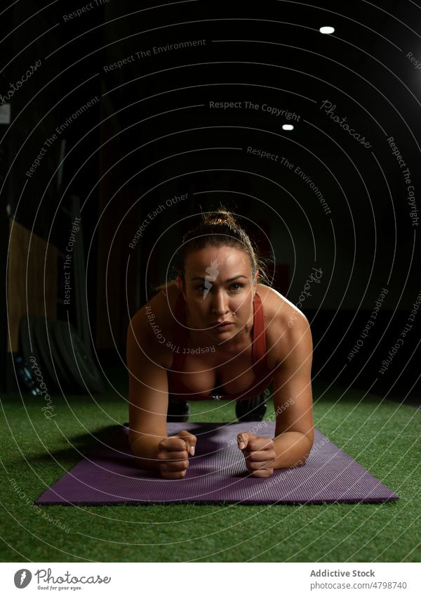 Slim woman in sportswear looking at camera while doing plank on mat in gym  stock photo