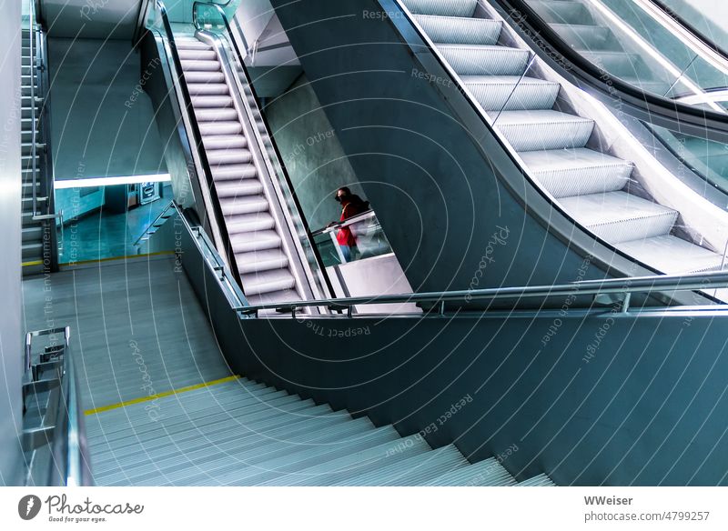 A system of stairs and escalators leads down into the depths, a young woman in a red jacket turns around Escalators Subsoil Tall Downward Upward Underground