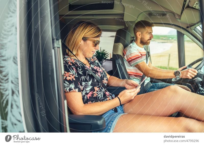 Couple traveling in camper van couple man driving woman looking mobile interior journey trip vehicle freedom 30s transport cellphone auto motor automobile