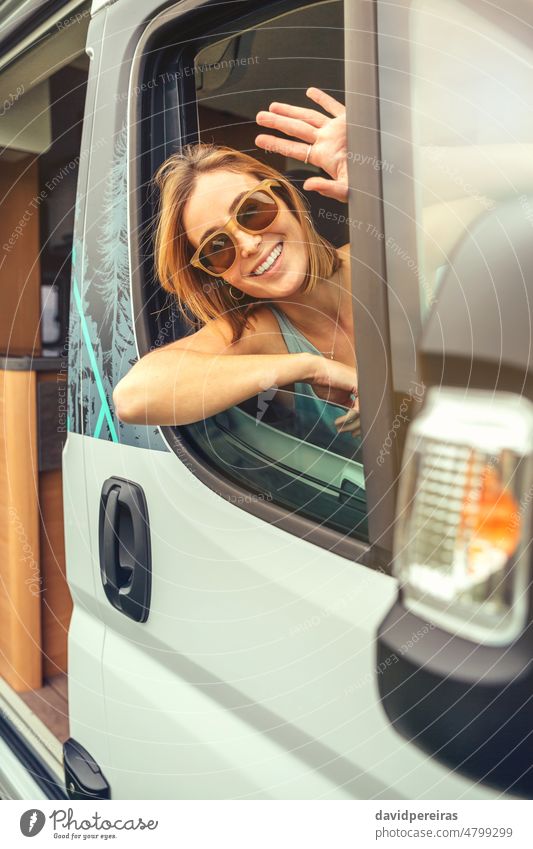 Young woman in sunglasses sitting in camper van happy young waving fun hand summer trip travel journey window vehicle freedom 20s person female tourist car