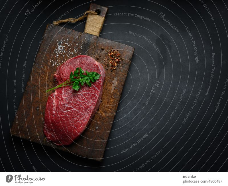 Raw beef tenderloin lies on a cutting board and spices for cooking on a black table, top view chop beefsteak bloody cow cuisine dinner filet fillet flat food