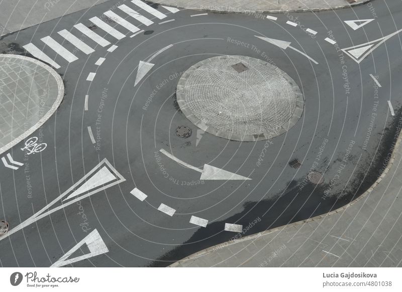 View from top on empty traffic circle or roundabout road with white arrows, crosswalk and other road signaling or marking in European town. Grey asphalt is partly wet after rain.