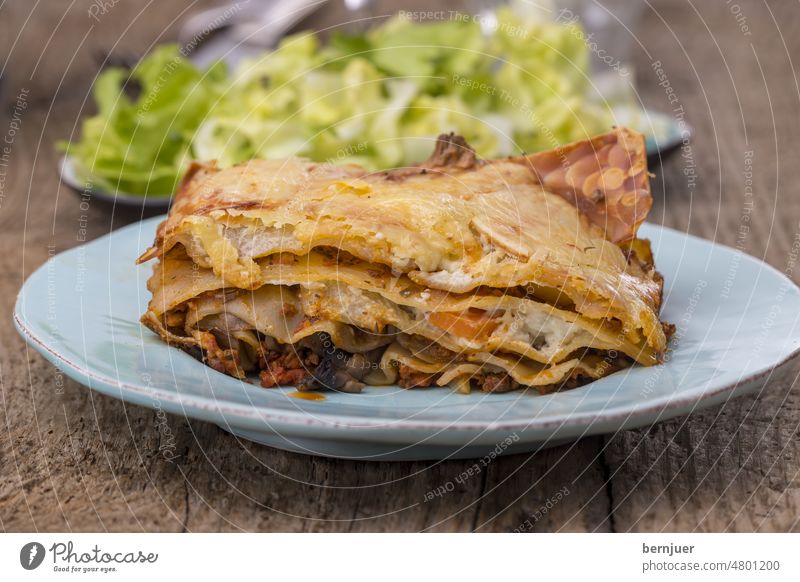 Lasagna with salad on dark wood Lasagne Knives Fork Vine Lettuce Wood Meal Eating Italian Kitchen pasta Rustic Plate Portion Cheese Beef Mediterranean Italy