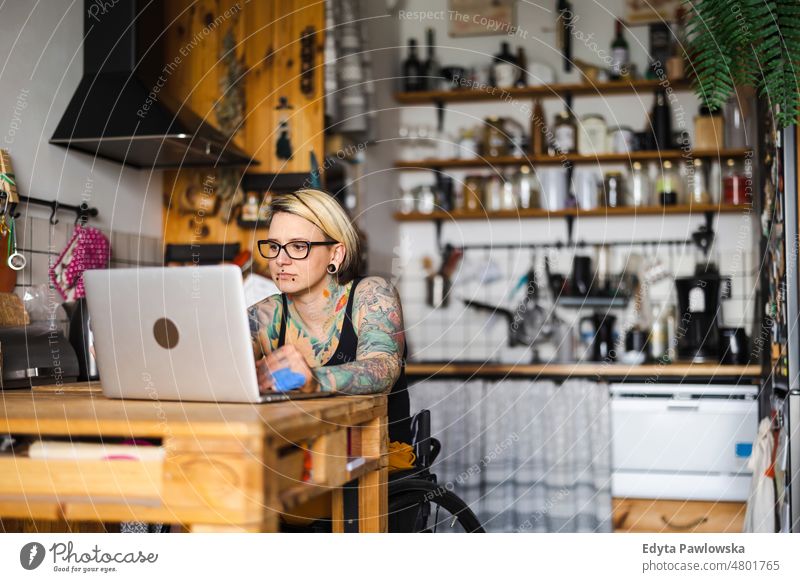 Young tattooed woman in a wheelchair working on laptop at home domestic life confidence indoors house people young adult casual female Caucasian attractive