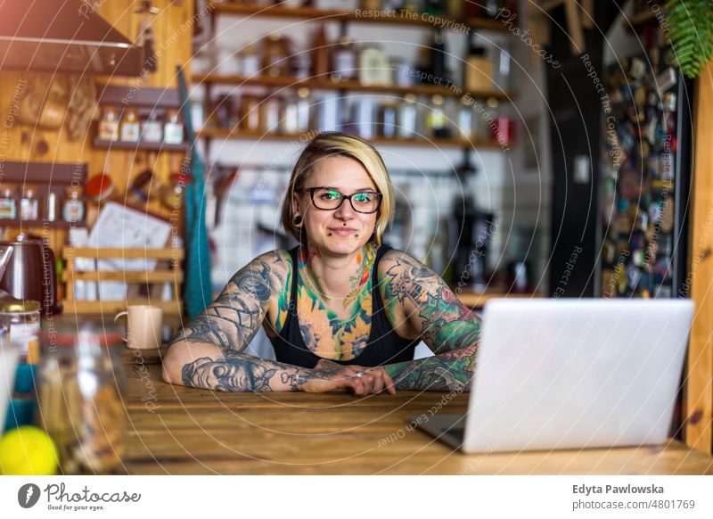 Tattooed woman working on laptop at home domestic life confidence indoors house people young adult casual female Caucasian attractive beautiful mobility tattoos