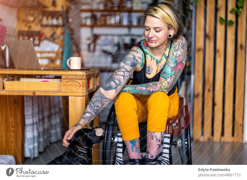 Young tattooed woman in a wheelchair with her dog at home domestic life confidence indoors house people young adult casual female Caucasian attractive beautiful