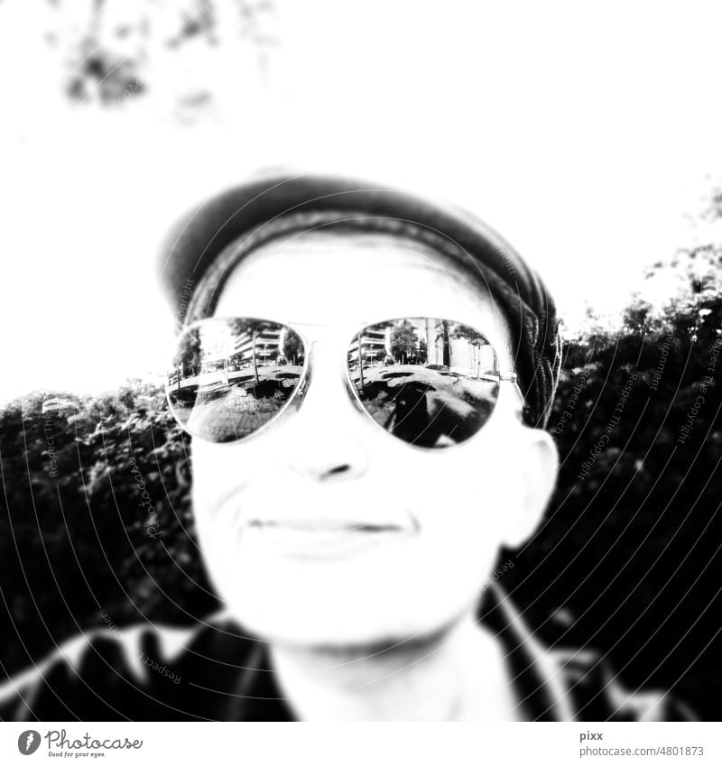 Friendly smiling person with sunglasses reflecting urban life. Wears slider cap. Black and white photo. Square Black & white photo Eyeglasses