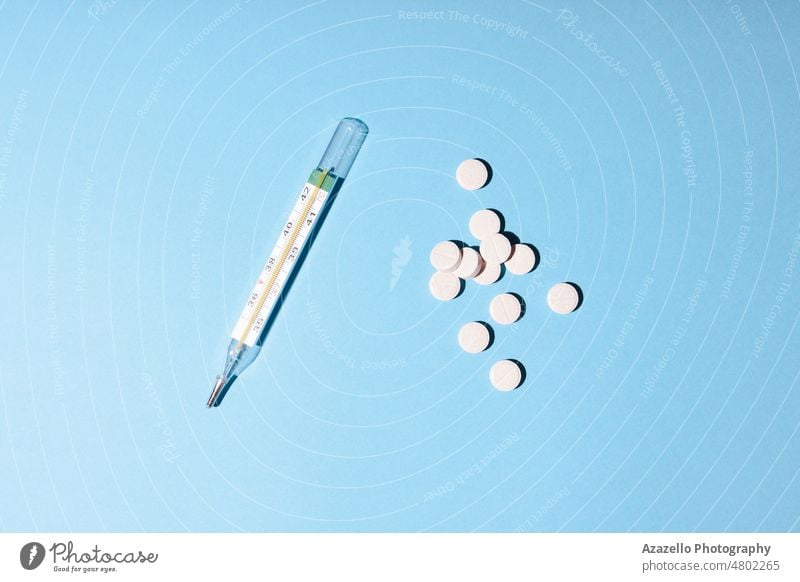 Minimalist medicine and healthcare concept flatlay pills and a thermometer on blue background. drugs chemistry pharmaceutical white tablet dose prescription