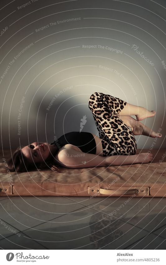 Young woman lying on leather sports mat with knees drawn up and wearing leopard print pants Woman pretty Feminine feminine Slim leop print Identity Authentic