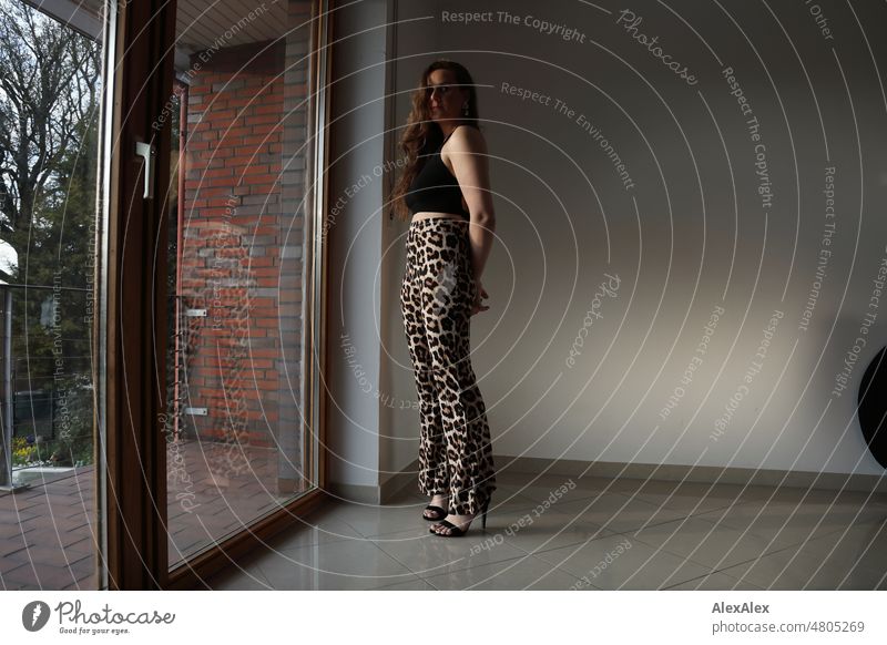 Young woman standing in front of balcony window wearing high heels and leopard print pants Woman pretty Feminine feminine Slim leop print Identity Authentic