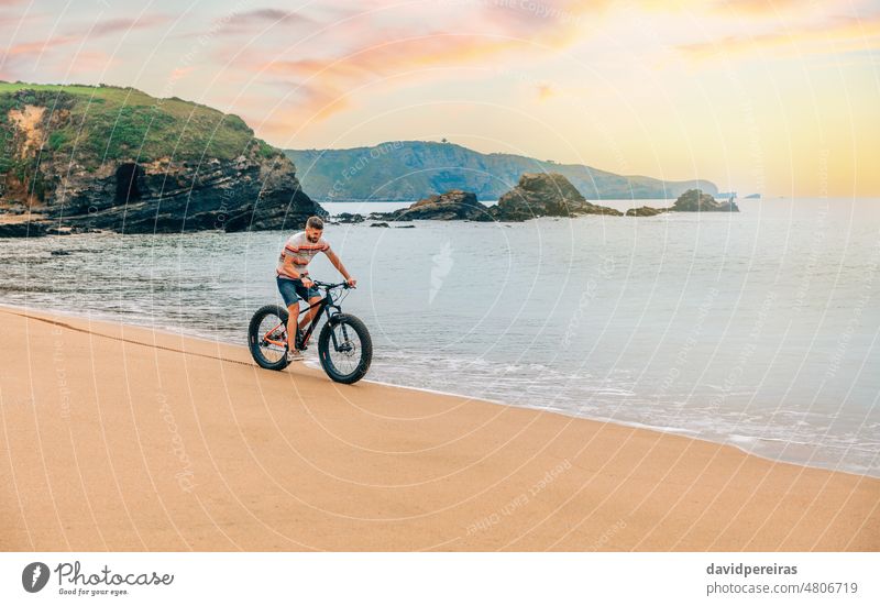 Young man riding a fat bike on the beach young seashore copy space smiling scenery landscape person sport bicycle lifestyle green active bicyclist male enjoy
