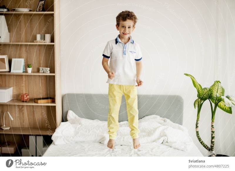 A little boy jumps on his bed in the bedroom and laughs. jumping young child home caucasian happy fun kid play childhood active person one playing playful