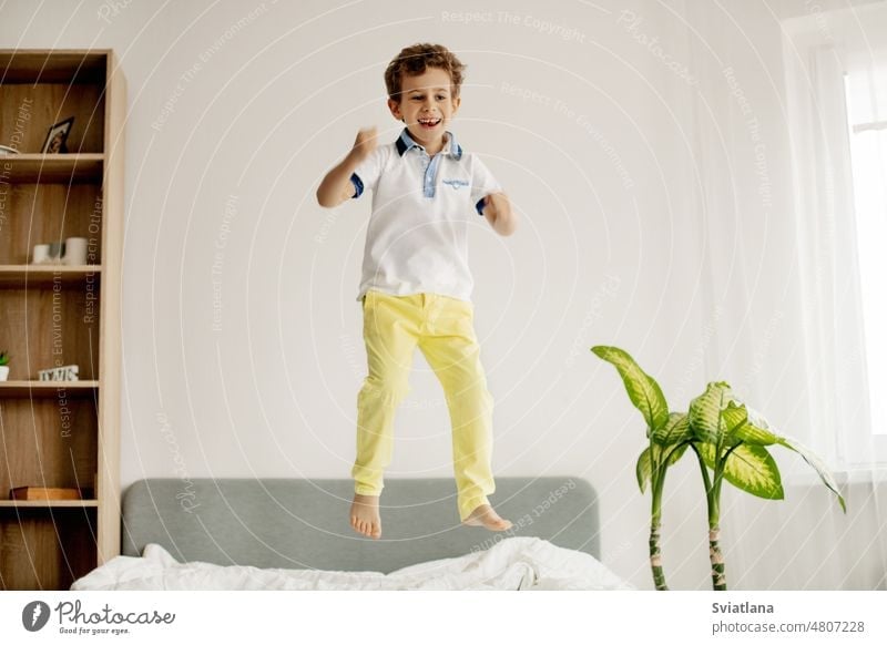 A little boy jumps on his bed in the bedroom and laughs. jumping young child home caucasian happy fun kid play childhood active person one playing playful