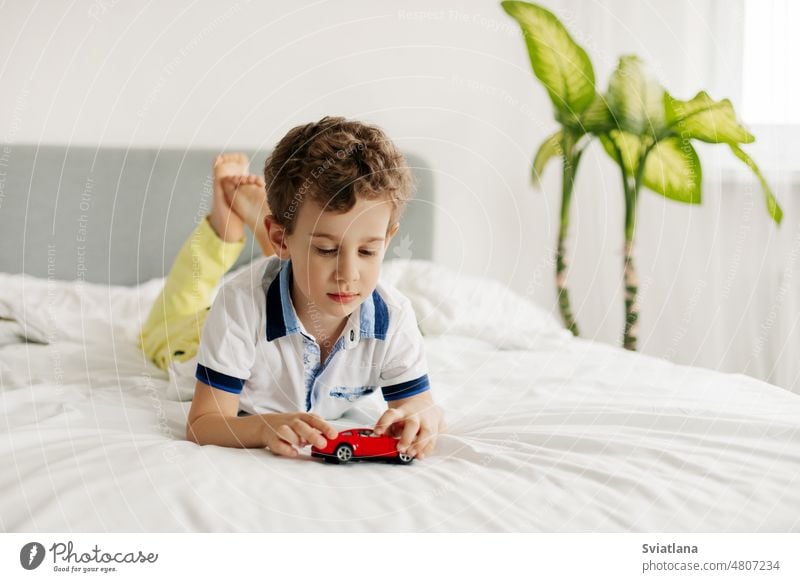 A little boy is lying on his stomach and playing with a toy car on his bed small game fun cute kid child young home caucasian happy adorable male bedroom family