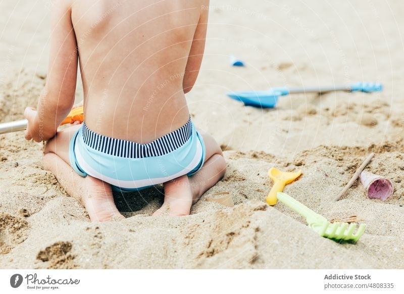 Crop boy playing on sand dig beach vacation summer weekend resort kneel child rest childhood shirtless holiday kid relax activity barefoot shovel travel