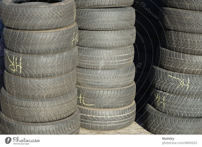 Stacked old car tires and winter tires on composite pavement in the sunshine in front of a car repair shop in Wettenberg Krofdorf-Gleiberg near Giessen in Hesse, Germany