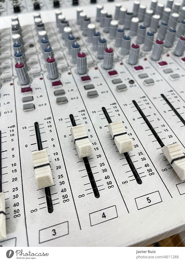 close up of the control knobs of a gray sound mixer table, with sliders and rotary knobs, vertical, background out of focus volume tremble bass eq equalizer