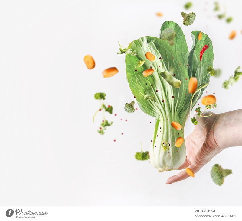 Women hand holding raw bok choy and flying vegetables at white background. women healthy food diet food levitation food organic broccoli carrots concept