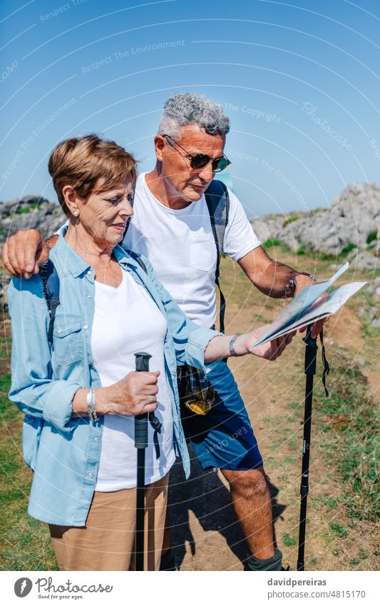 Senior couple with poles trekking looking map senior cheerful embracing smiling man woman excursion person lifestyle vacation hiker elderly adult mature nature