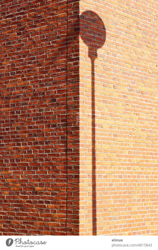 Shadow of round traffic sign with pole on the corner of a building made of red bricks, half of which is in the shade / minimalism Road sign Shadow play Geometry