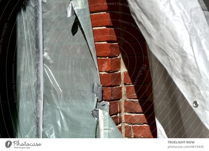 Grey dust protection tarpaulin partially opened during facade renovation gives view of red brick masonry refurbishment Facade protective tarpaulin bricks