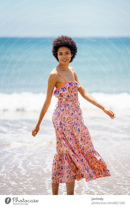 Happy black woman in summer dress, walking on the sand of a tropical beach. afro hairstyle relax coast curly background beautiful person girl positive happiness