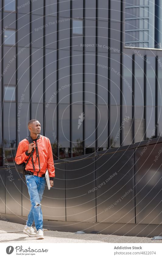 Confident black male student strolling near modern building in city man walk street backpack laptop confident serious trendy urban generation z contemporary