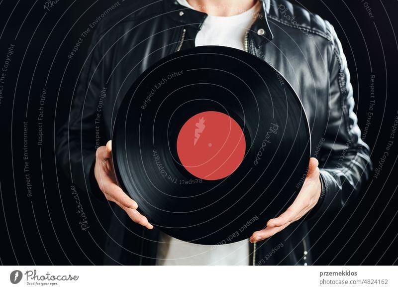 Man holding vinyl record. Vintage music style. Rock style male wearing black jacket holding black disc standing on dark background. Retro music disco sound