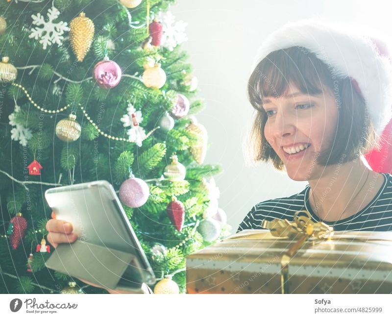 Smiling woman holding wrapped gifts using tablet near christmas tree presents happy buying online smiling stacked home holiday santa mom new year device winter