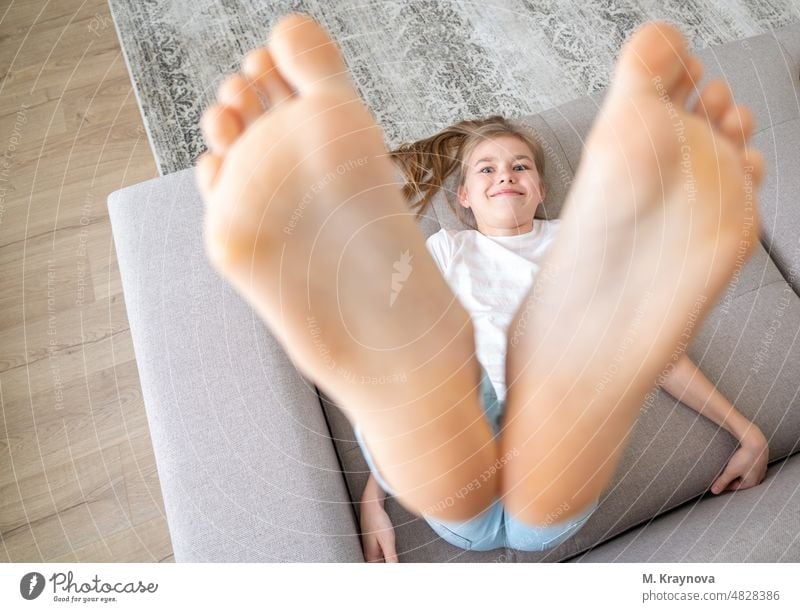 Preteen girl lying on couch with her bare feet raising up high foot relaxation barefoot person child bed comfortable resting female happy home morning closeup
