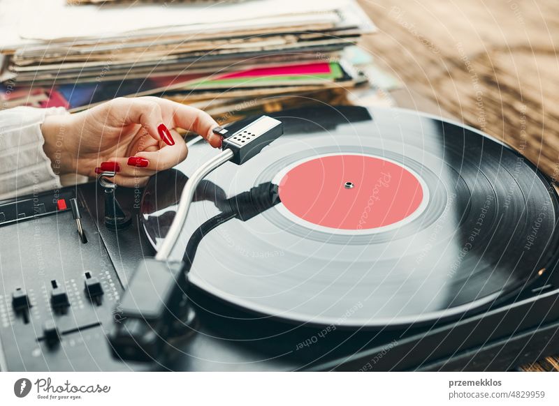 Young woman listening to music from vinyl record player. Playing music on turntable player. Female enjoying music from old record collection at home analog