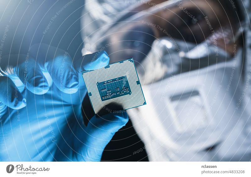 Ultra Modern Electronic Manufacturing Factory, Engineer in Sterile Coverall Holds Microchip with Gloves and Examines it semiconductor microchip manufacture