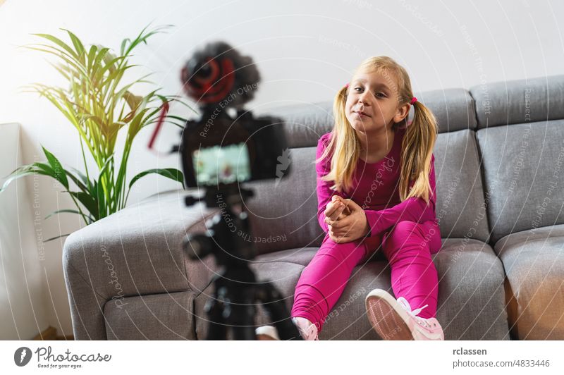 Beautiful young girl in pink casual wear smiling at camera and talking on video shooting with technology. Kids Social media influencer or young content maker concept in relax casual style at home.
