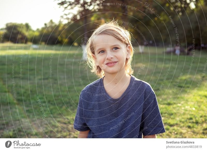 Teenger boy looking at camera outdoor close-up lifestyle portrait in the park in nature. Green grass backgrund Golden hour sun light teen face young happy fun
