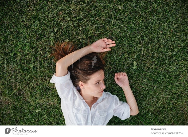 shot of woman lying on green grass above adult caucasian daydreaming female garden girl hands happy leisure lifestyle meadow nature outdoors outside park