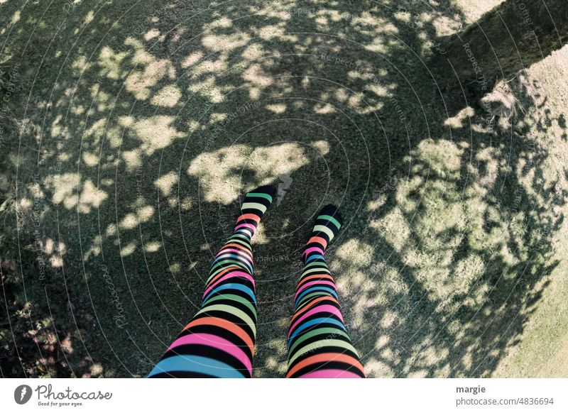 A girl with colorful striped stockings stands on the shadow of a