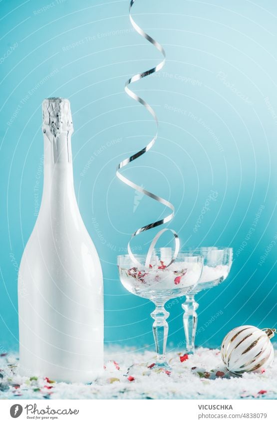 Christmas and New Year setting with champagne bottle, glasses, falling silver ribbon, snow and bauble and at light blue background. christmas new year