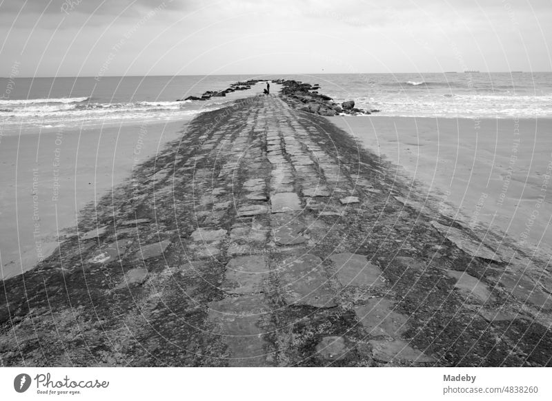 Stones and masonry as a dam and breakwater for coastal protection in rainy weather on the beach in Knokke-Heist on the North Sea near Bruges in West Flanders in Belgium, photographed in neorealist black and white